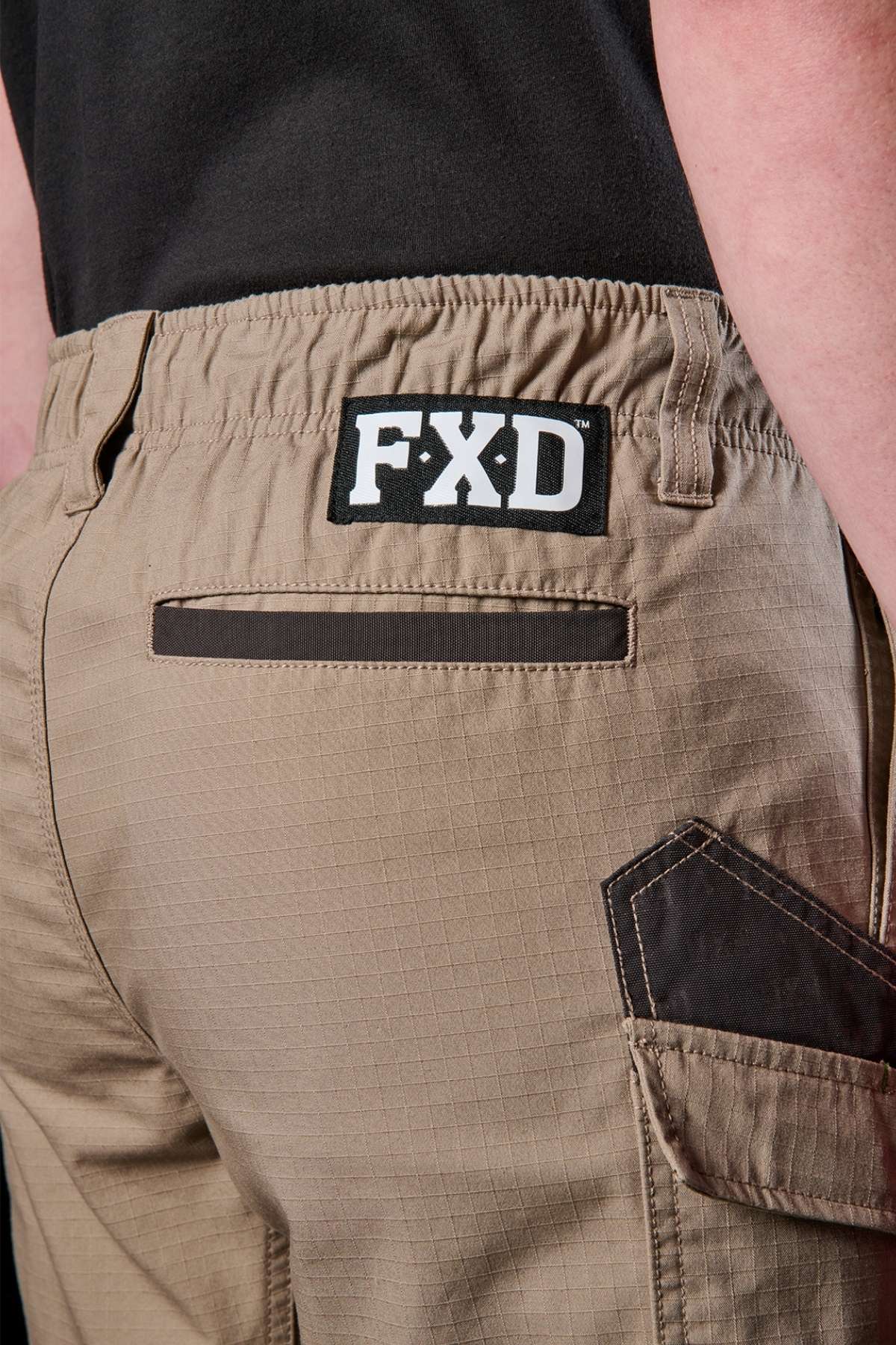 Close-up of a person wearing the FXD WS-7 Work Short in tan, showcasing the black "FXD" logo on the waistband. These shorts are designed with a back pocket, reinforced stitching, and offer utility while maintaining comfort.