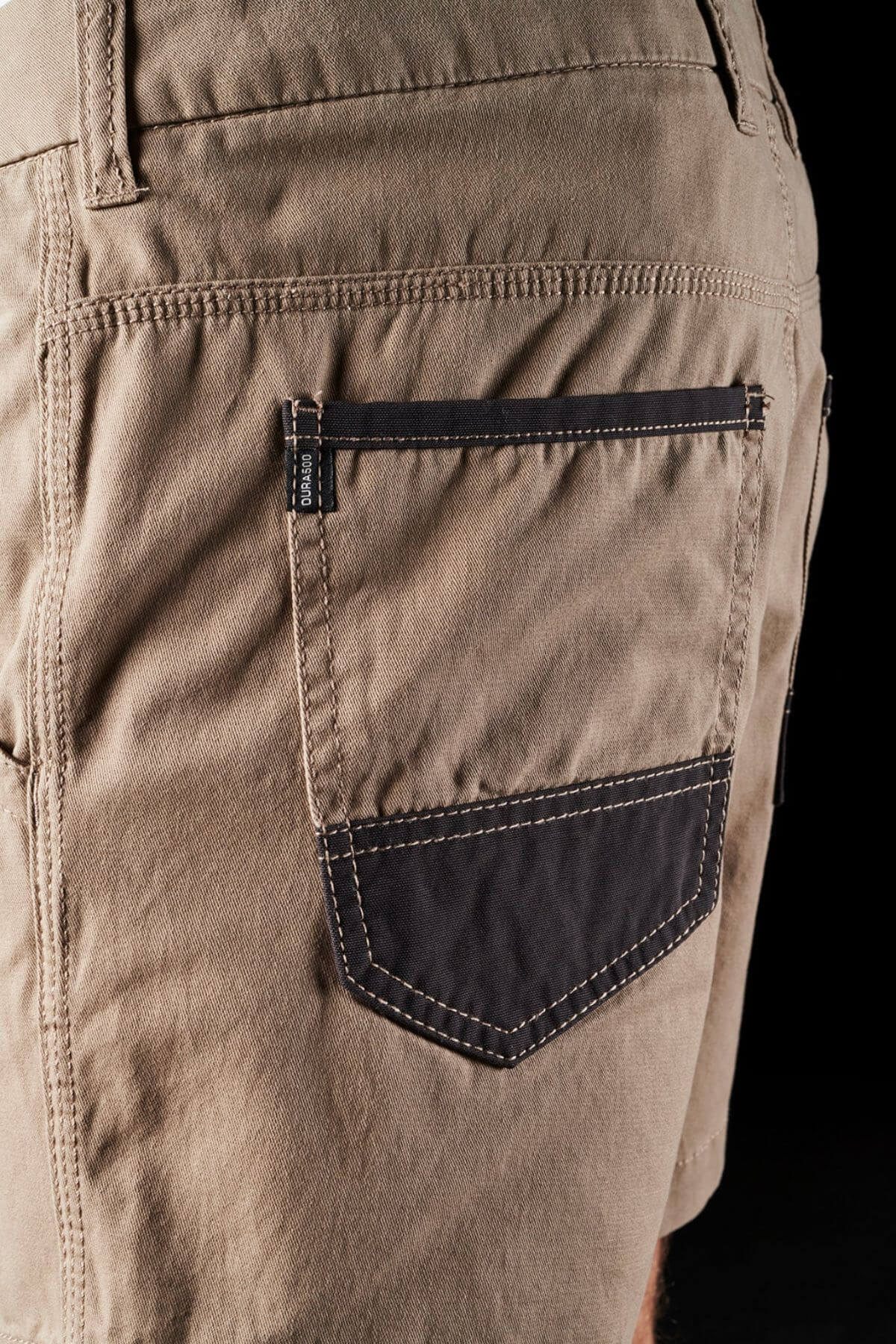 Close-up image of the back pocket of a pair of FXD WS-2 Short Short, showcasing a contrasting black pocket flap and reinforced stitching. The detailed stitching and soft touch cotton twill fabric texture are prominently visible, along with a small logo tag on the pocket seam.