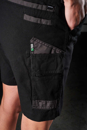 Side view of a person wearing FXD Womens WS-3W Shorts in black, featuring DURA500 reinforced pockets with a small "PRO" tag on one of them. The person's hand is partially inside one of the pockets, and the image highlights the detailed stitching and durability of these stretch work shorts.