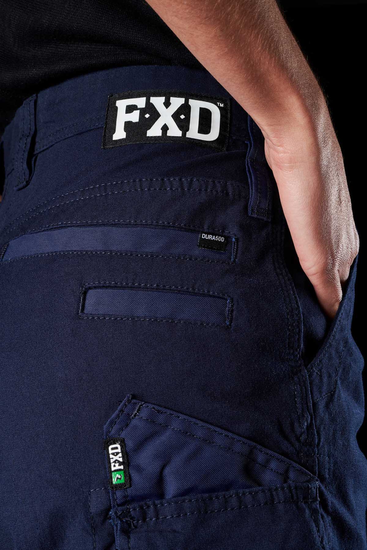Close-up of a person wearing navy blue FXD Womens WS-3W Shorts. The shorts feature DURA500 reinforced pockets and triple needle seams, including a visible FXD label on both the waistband and a side pocket. The person's hand is partially visible, resting on their hip.