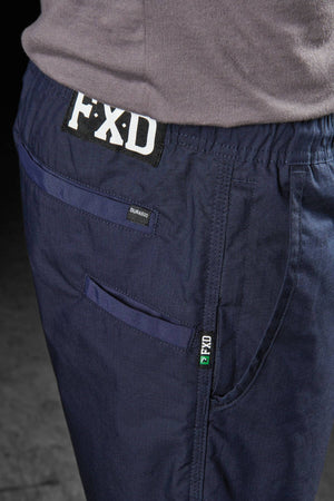 Close-up of a person wearing blue FXD WS-4 Shorts, focusing on the back pocket area. The brand's name, "FXD," appears prominently above the pocket, and the "Durable" tag is visible below it. Featuring a comfort stretch waistband and a stitched-on green label with the FXD logo for added comfort.