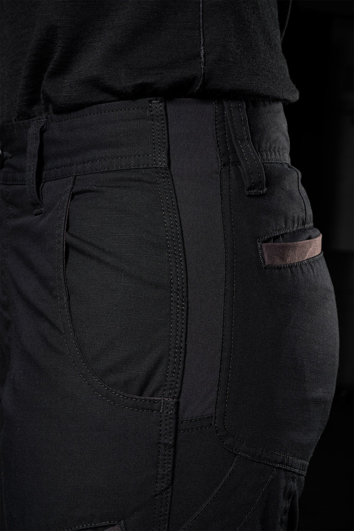 Close-up of a person wearing FXD Womens WP-7W pants, with the focus on the side pocket and part of the leg. The pants have a sleek design with visible stitching and slightly textured fabric, offering flex double weave for comfort. The person is also wearing a dark top tucked into the pants.
