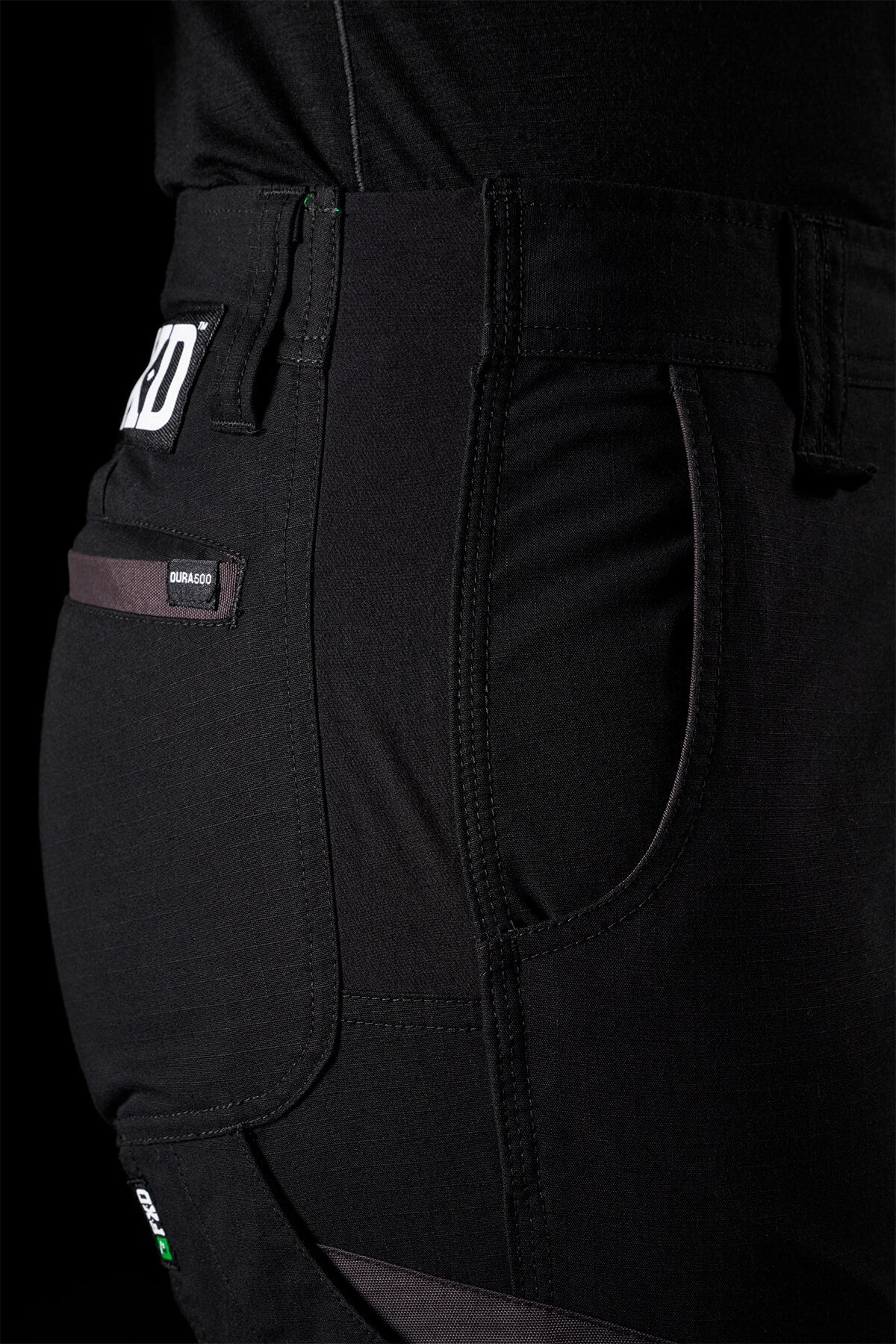 Close-up view of FXD Women's WP-8W black work pants showcasing details like a side pocket, belt loop, and a small tag labeled "Dura360." The fabric looks durable and is probably intended for heavy-duty use, as evidenced by the abrasion panels and material texture.