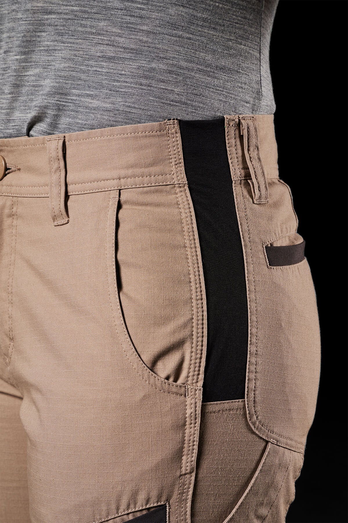 Close-up of a person wearing FXD Womens WP-8W light brown cargo pants that feature a black stretch waistband and are paired with a gray shirt. These lightweight stretch ripstop pants boast multiple pockets, belt loops, and detailed stitching along the seams, ensuring maximum range of movement.