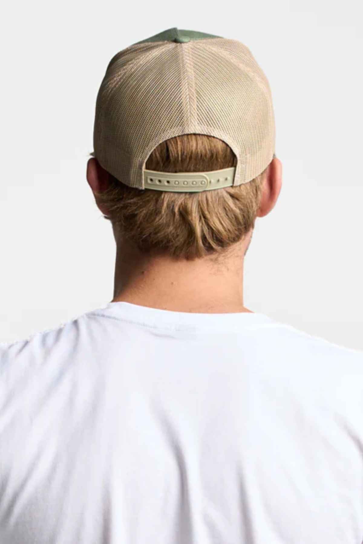 A person sporting a FlexFit American Stitch Trucker Cap in beige, worn backward with a snapback strap, paired with a white T-shirt. The image focuses on them from the back, emphasizing the cap and their light brown hair.