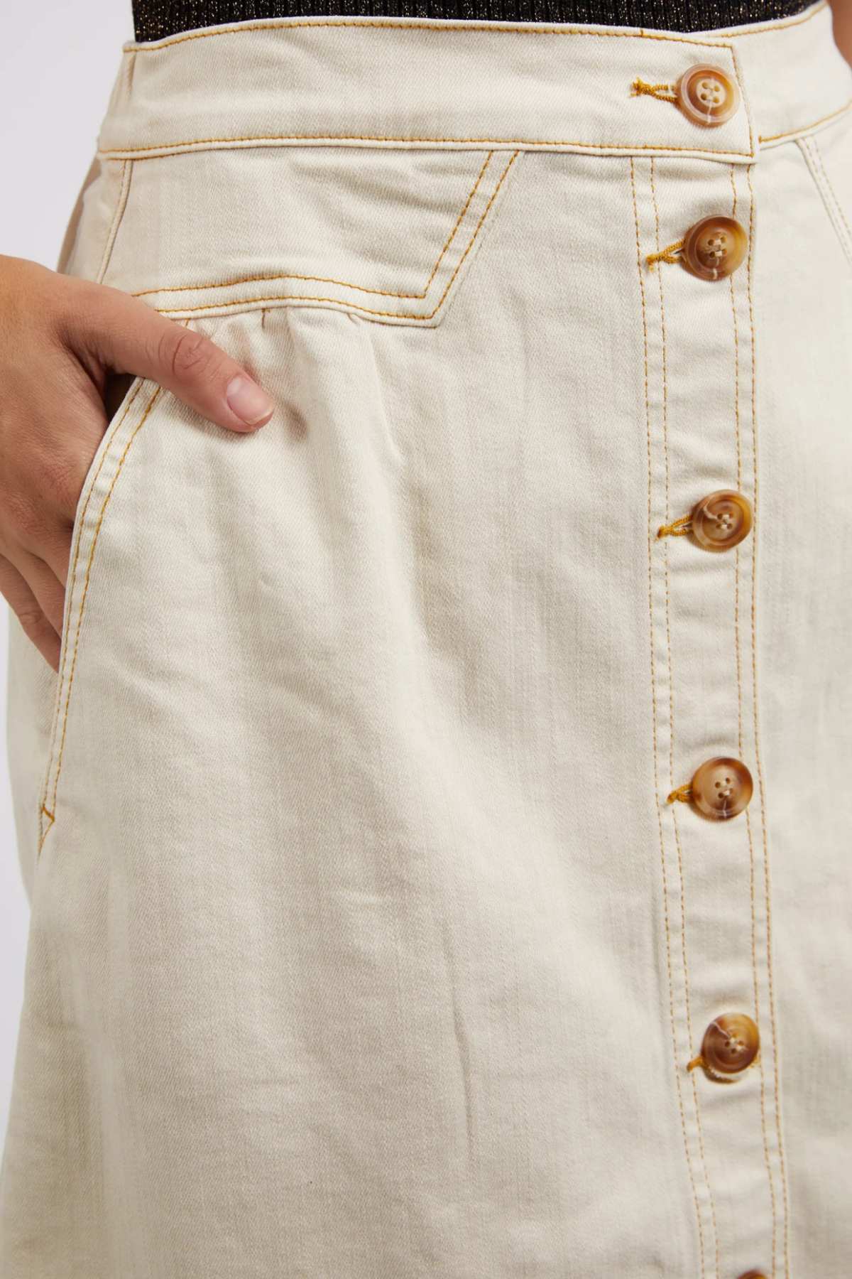 Close-up of the Foxwood Amanda Skirt—an A-line design in cream, featuring brown front buttons, yellow stitching, and a hand tucked in the side pocket for a retro-inspired look.