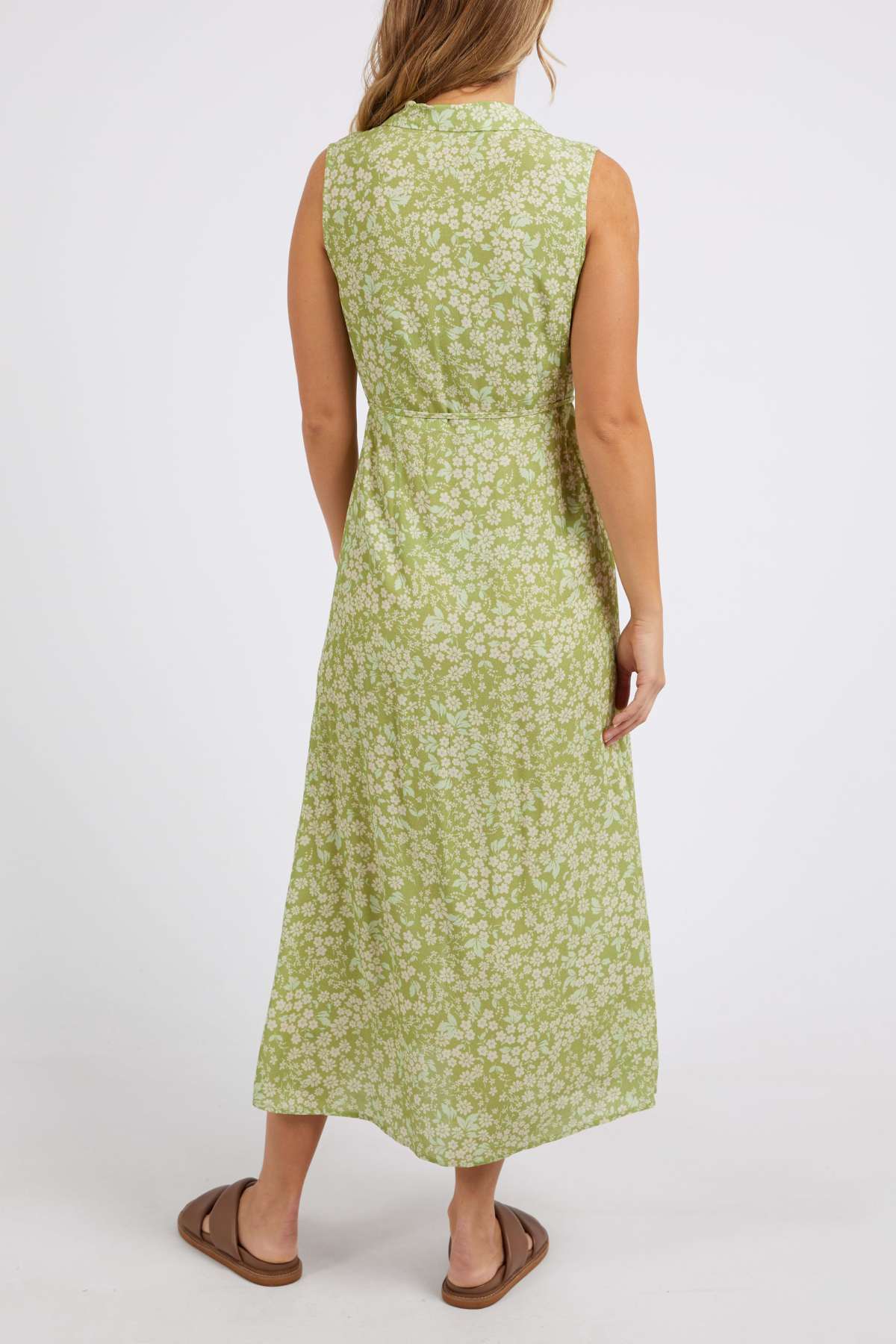 Wearing the Foxwood Anatayla Floral Dress made from lightweight fabric ideal for warm weather occasions, the individual is photographed from behind. The long, sleeveless green dress is complemented by brown sandals against a simple white background.