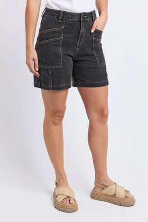 Wearing Foxwood Balmy Short in washed black with visible stitching, paired with a white top and beige sandals, a person stands against a plain background, one hand in their pocket.