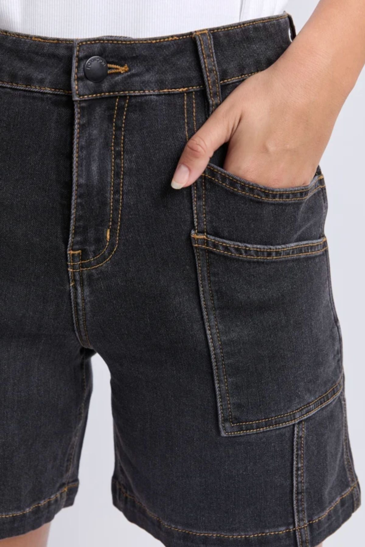 Close-up of a person wearing the Foxwood Balmy Short in washed black with orange stitching, paired with a white top and their right hand in the pocket—showcasing an effortlessly stylish and comfortable look.
