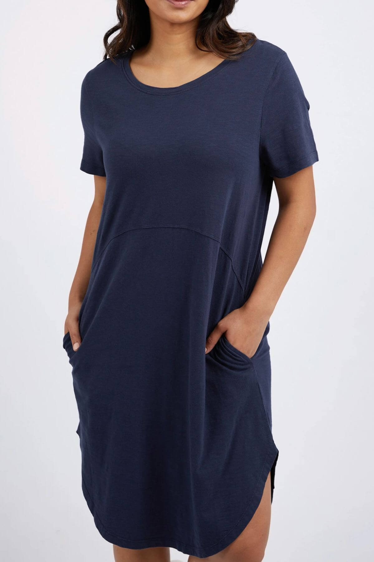 A model showcases the Foxwood Bay Dress, a navy blue jersey design with short sleeves, a round neckline, and pockets. Made of cotton for comfort, it has a relaxed fit ideal for casual wear. The hemline is just above the knees against a plain white background.