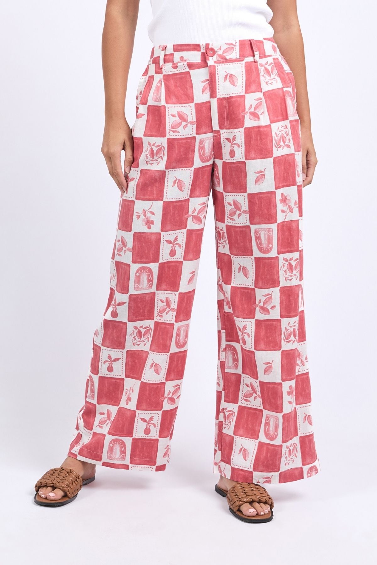 Someone pairs the Foxwood Biarittz Pant—featuring a red and white check in a linen-viscose blend with unique motifs—with a white top and brown woven sandals.