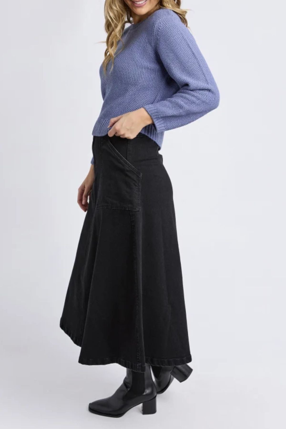 A woman wearing the Foxwood Blair Long Sleeve Knit in light purple, a long black A-line skirt, and black heeled boots stands sideways and smiles.