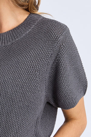 Close-up of a person wearing the Foxwood Blair Short Sleeve Knit, showing its detailed knit pattern and relaxed fit on the upper chest and arm, with light brown hair visible at the top.