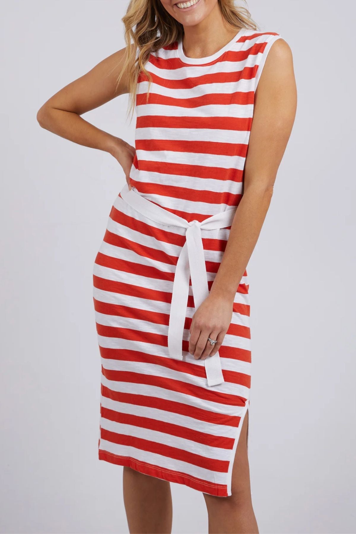 A woman wears the Foxwood Bondi Stripe Dress, a sleeveless, knee-length style with red and white horizontal stripes and a white waist tie that flatters her figure as she smiles against a plain background.
