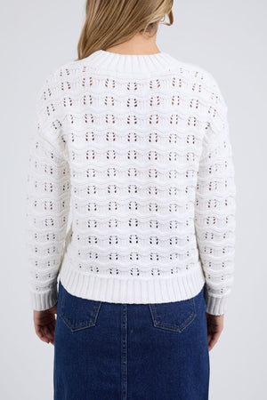 A person with blonde hair, wearing the Foxwood Carter Knit sweater in white and a blue denim skirt, is shown from the back against a plain light gray background.