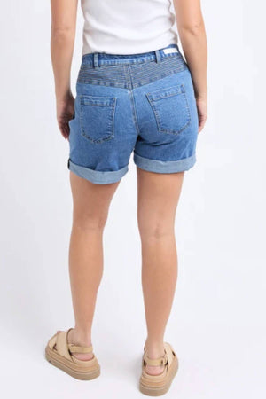 A person stands with their back to the camera, wearing a white top, Foxwood Devi Short in rolled-up blue denim, and beige platform sandals against a plain white background.