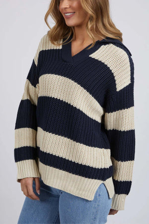 A woman in the Foxwood Estella Stripe Knit—a navy and beige chunky yarn-dyed cotton-acrylic sweater with a v-neckline—paired with light blue jeans, stands against a plain background.