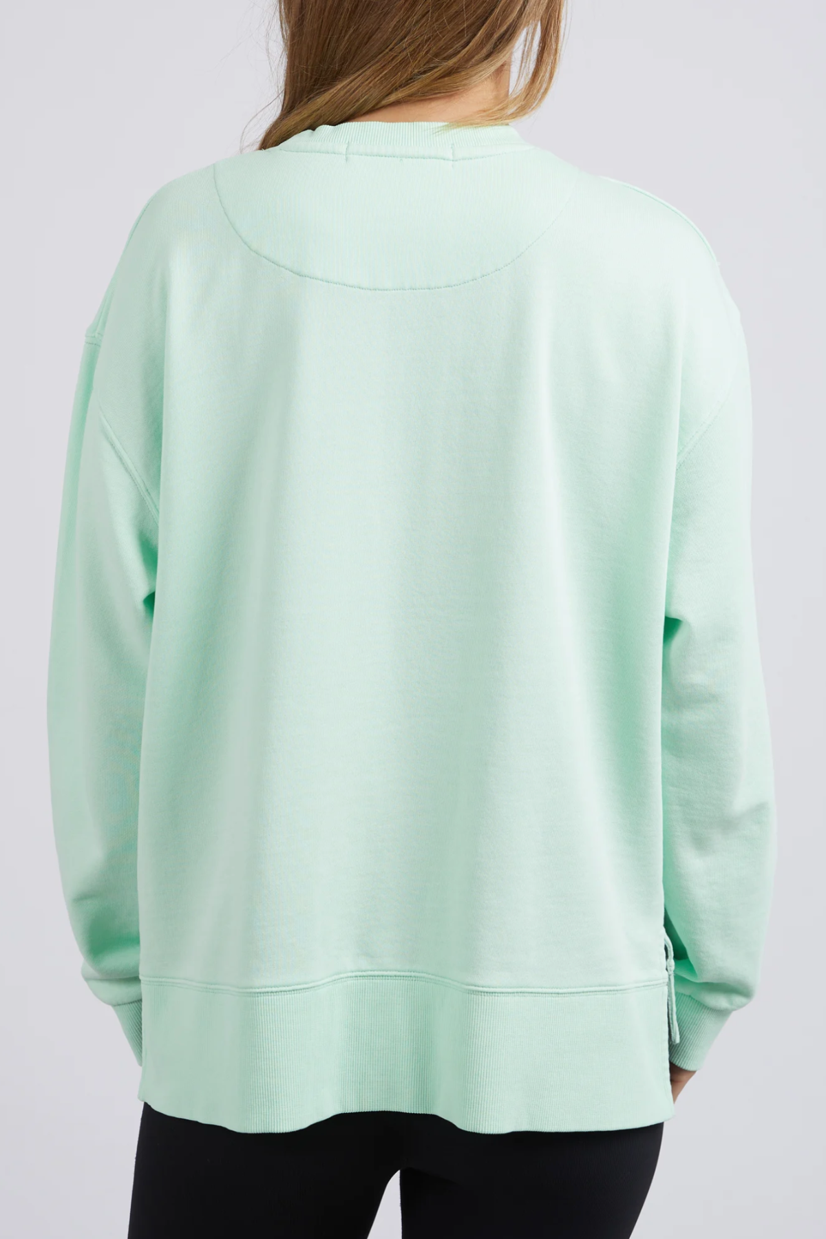 Someone with long hair wears an oversized Foxwood Glider Crew in light green, showcasing a relaxed fit made from 100% cotton. They're paired with black pants and face away against a plain white background.