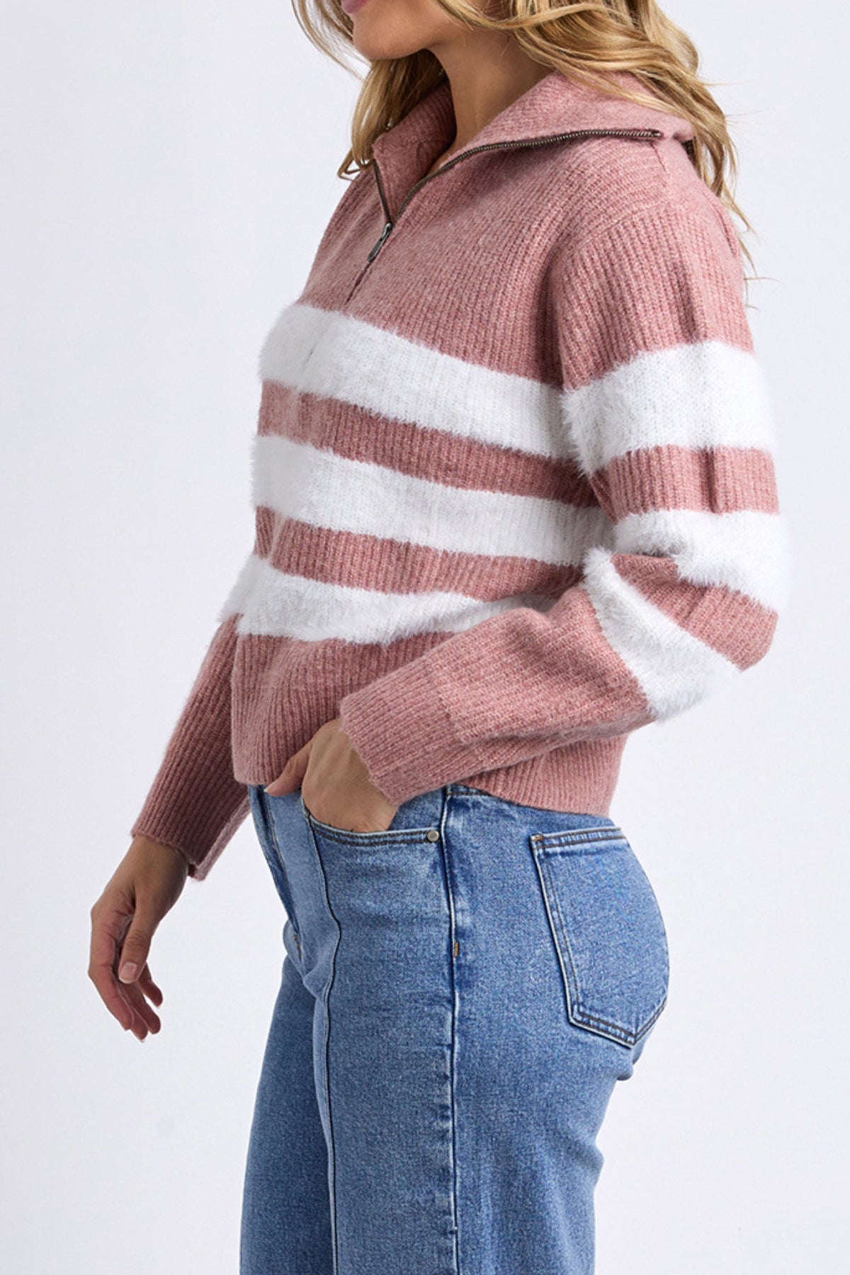 A woman wearing the Foxwood Gracie Zip Crew, a pink and white striped knit zip-neck sweater, with blue jeans stands with one hand in her pocket against a plain background.