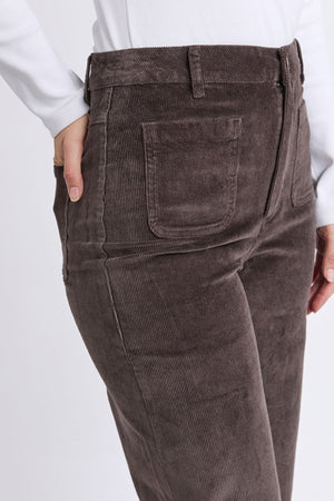 A person wearing the Foxwood Henrietta Cord Pant in brown, styled with a white long-sleeve top; image focuses on the front pocket and textured corduroy fabric, shown from the waist down.