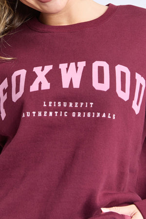 Wearing the Foxwood Intention Crew—a relaxed fit, maroon cotton-rich fleece sweatshirt featuring "FOXWOOD" in bold pink letters with "LEISUREFIT AUTHENTIC ORIGINALS" printed below.