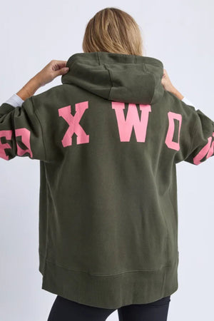 A person with blonde hair wears a relaxed, oversized olive green Foxwood Interval Hoodie with the hood up. Bold pink "FOXWOOD" lettering on the back and sleeves adds standout style, ideal for everyday comfort and wear.