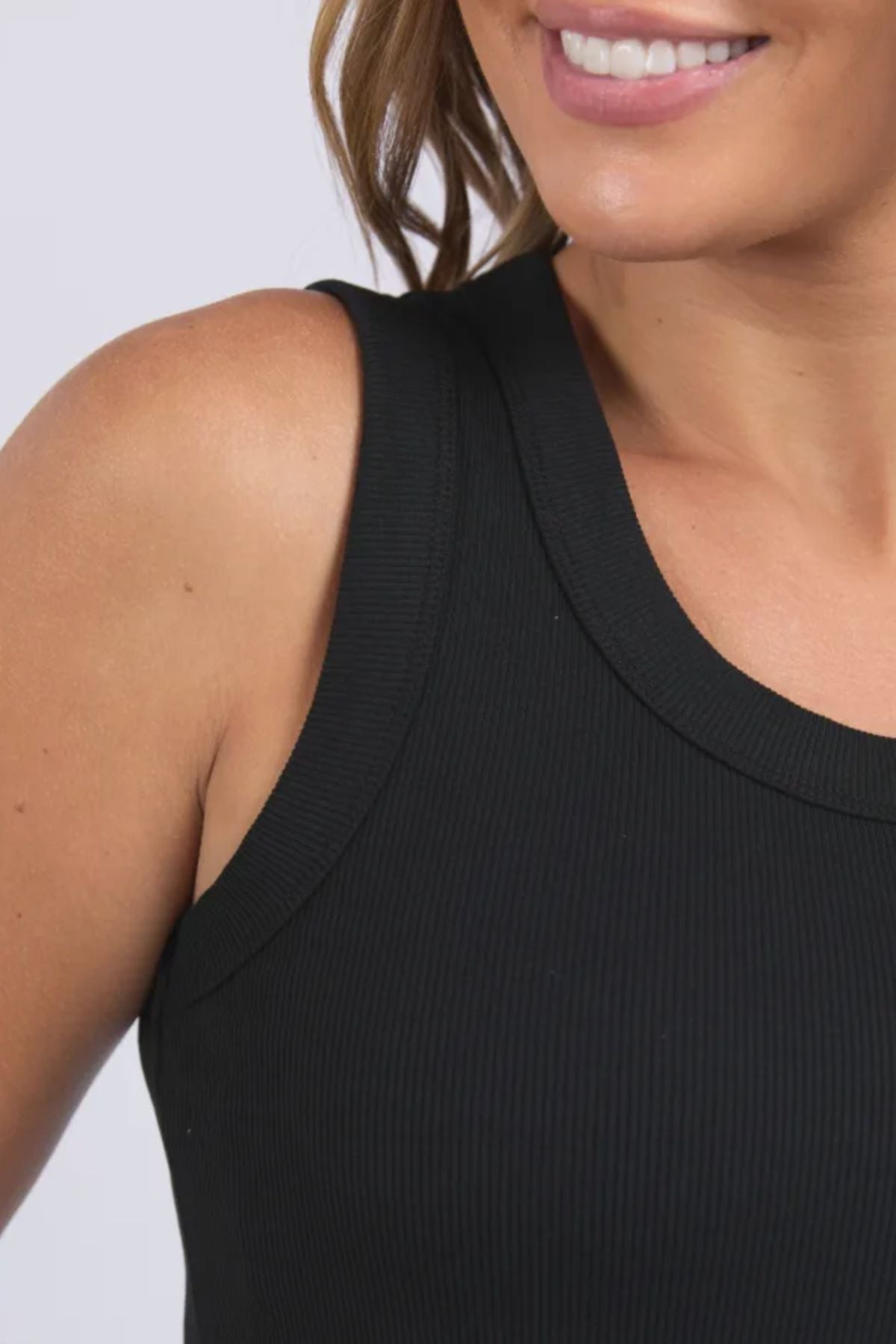 A close-up shows a woman smiling in the Foxwood Iris Tank, featuring black ribbed stretch fabric, with her wavy hair draped to the side and part of her shoulder visible.