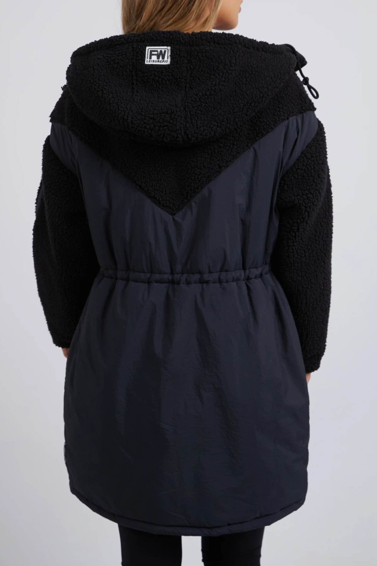 Seen from behind, the Foxwood Longline Anorak features two-tone design with a textured upper and smooth lower section. Ideal for outdoor adventures, this coat is made from durable nylon polyester blend in black, with a drawstring waist and hood adorned by a small logo.