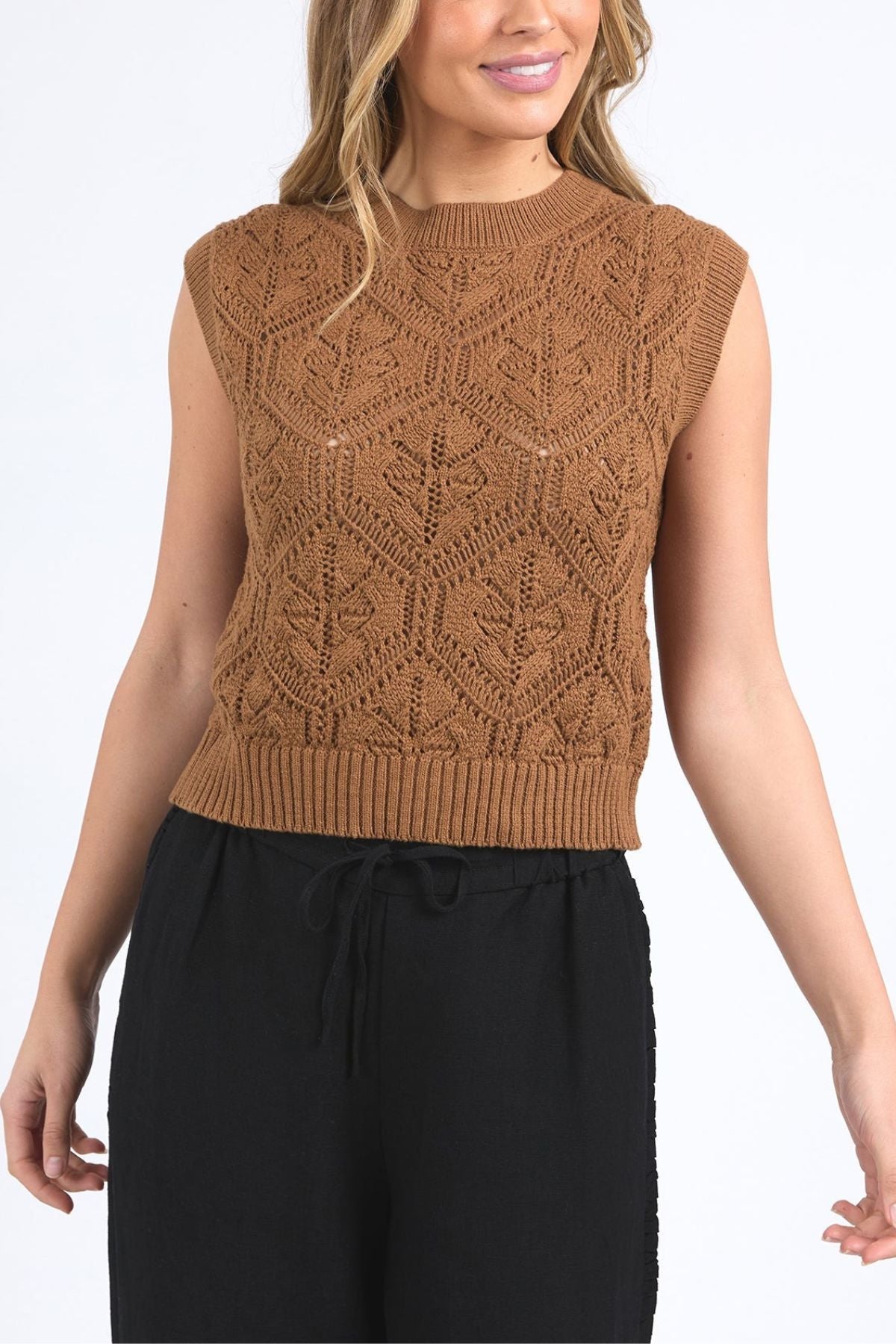 A woman wearing the Foxwood Luna Knit Vest—a sleeveless brown pointelle top with a geometric pattern—and black drawstring pants, standing against a plain white background.