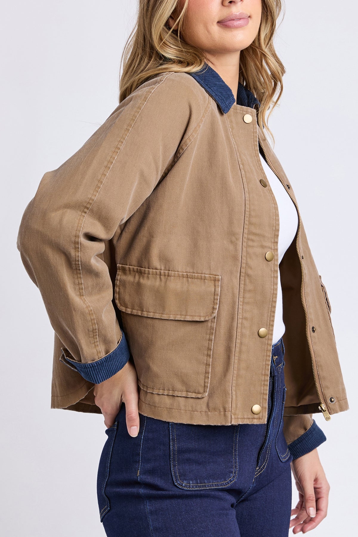 A woman wearing the Foxwood Colwood Jacket, a sporty style with front pockets and contrast collar and cuffs, paired with high-waisted dark blue jeans. She poses with one hand on her hip.