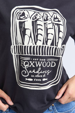 Wearing the Foxwood Pesce Tee—a 100% cotton, coastal-inspired shirt—features four sardines in a tin can and "Foxwood Sardines in olive oil EST 2018 FXWD" below the illustration.