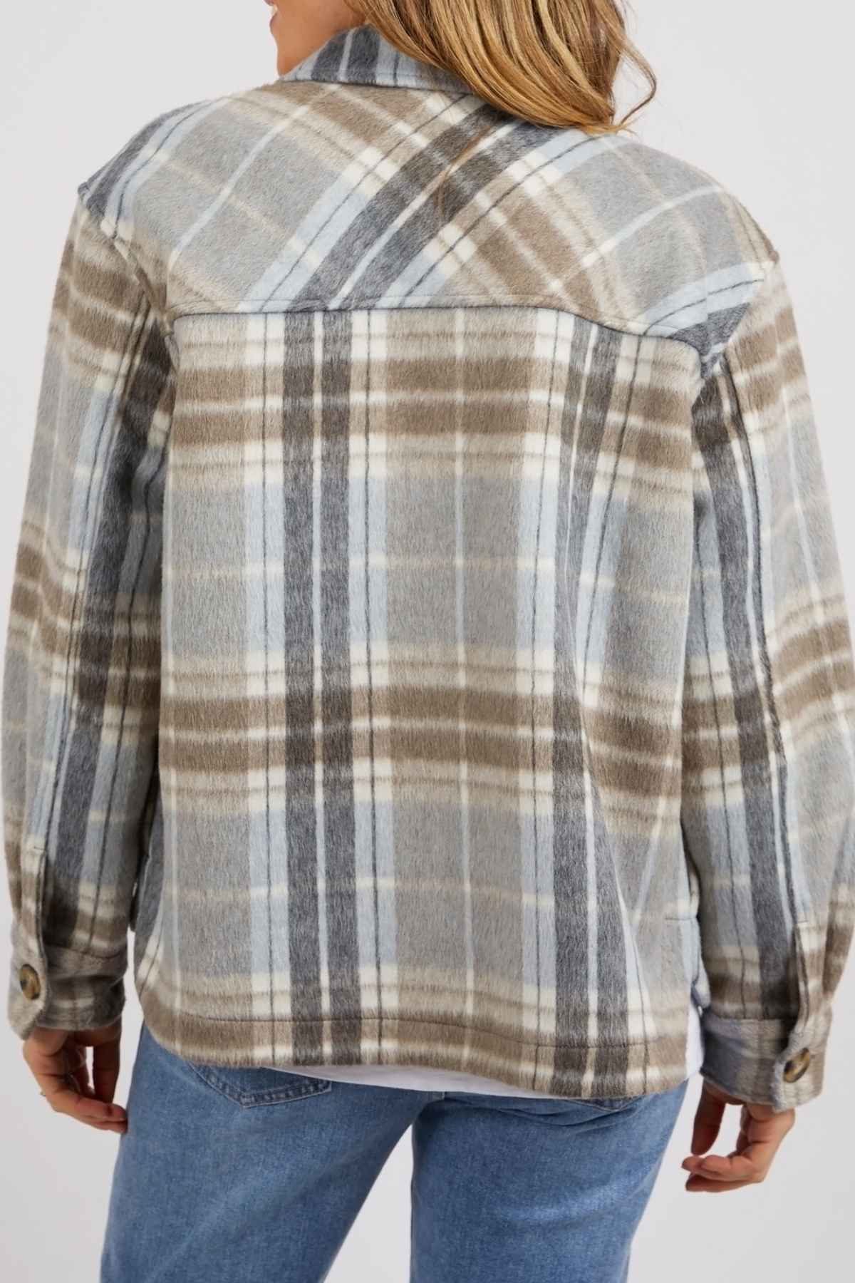 A person with medium-length hair, viewed from the back, wears blue jeans and a Foxwood Rhodes Check Coat in light gray, brown, and white with a yarn-dyed check pattern.