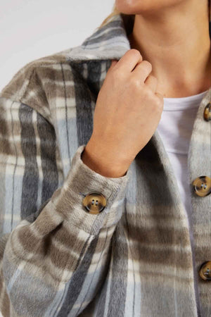 A person in the Foxwood Rhodes Check Coat, with a cozy gray and beige check wool blend, over a white top. They hold the collar with one hand while their face is partially out of frame.