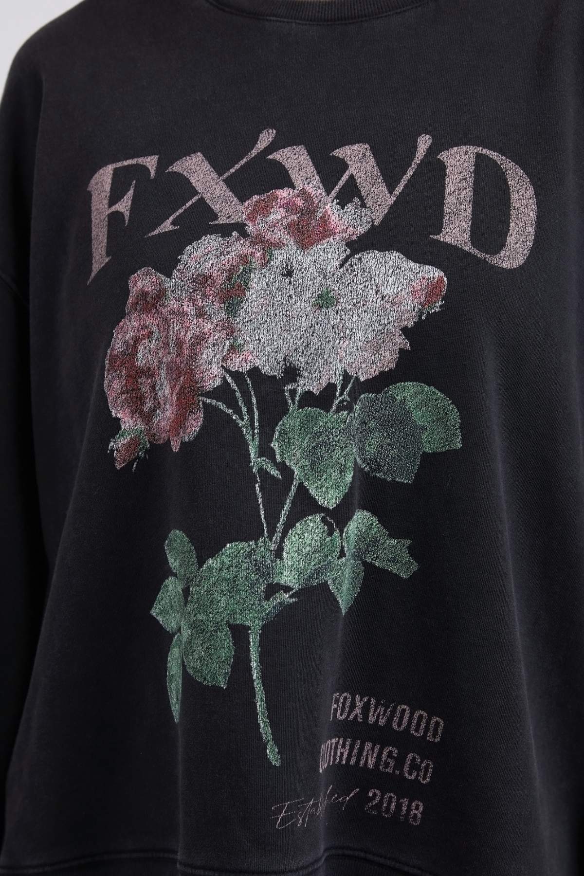 The Foxwood Rosa Crew is a black, 100% cotton sweatshirt featuring an embroidered "FXWD" chest print above a colorful floral graphic, with "FOXWOOD NOTHING CO" and "Est. 2018" elegantly displayed at the bottom.