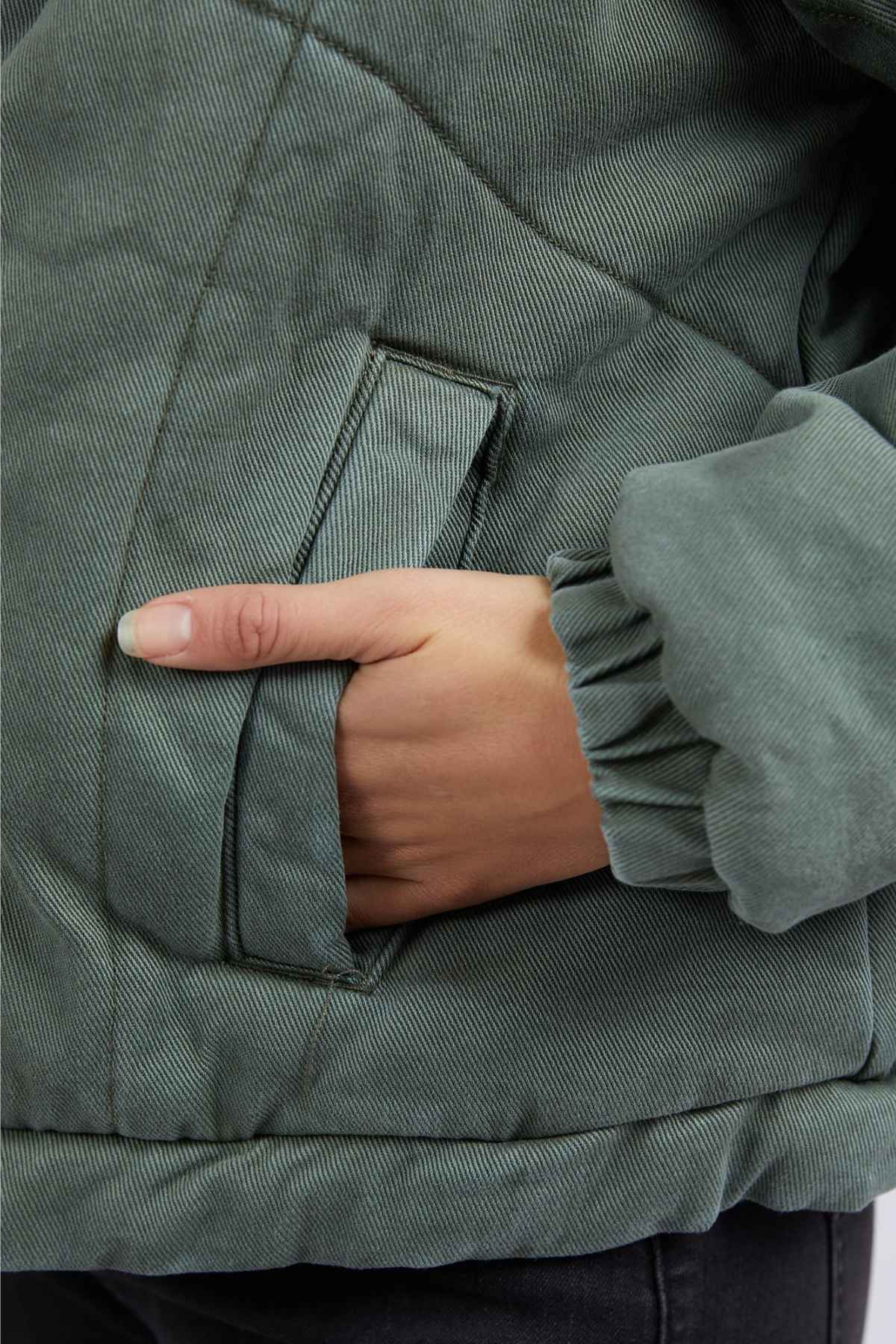 A close-up of a hand inside the pocket of the Foxwood Rosalee Denim Jacket, featuring a green quilted pattern, elastic sleeve cuffs, and cozy cotton denim for added comfort.