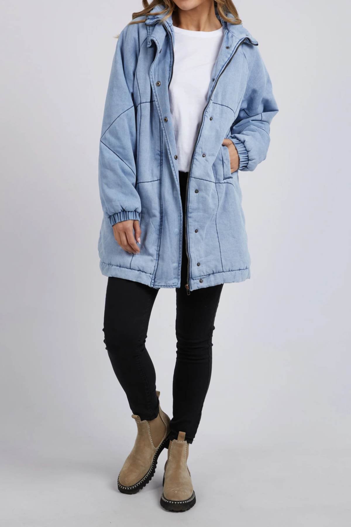 A person in a light blue Foxwood Rosalee Longline Jacket, white t-shirt, black skinny pants, and tan ankle boots stands against a plain light background with their face partially out of frame.