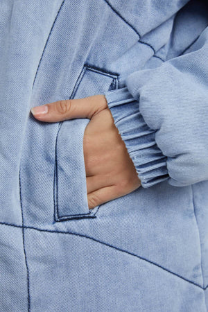 A close-up shows a hand partly tucked in the pocket of the Foxwood Rosalee Longline Jacket, made from 100% cotton vintage washed denim, featuring dark stitching and a ribbed sleeve cuff.