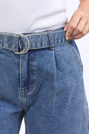 A person wears high-waisted blue Foxwood Saint Shorts with a silver D-ring belt, holding the waistband with one hand, paired with a white ribbed shirt.
