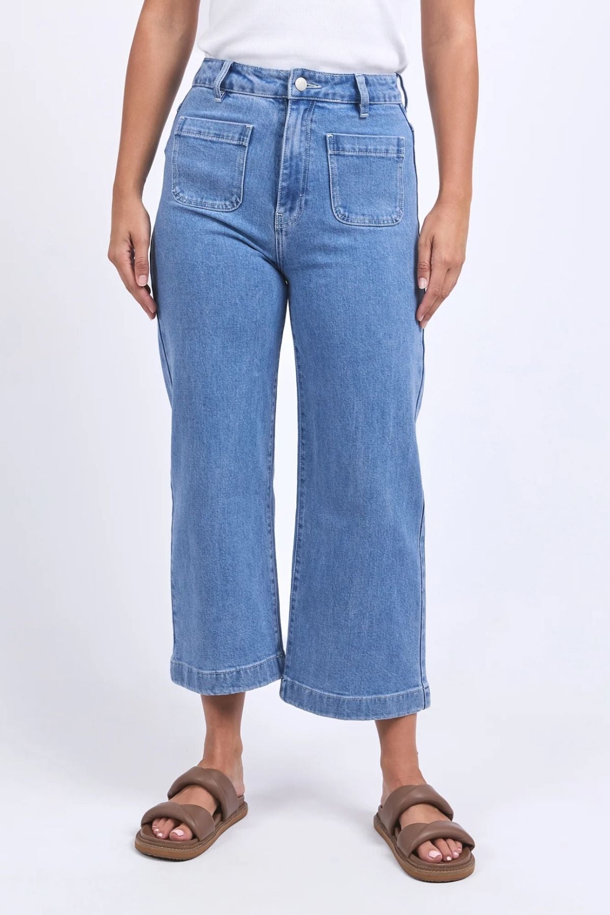 Someone wears the Foxwood Sarah Crop Jean, a high-rise wide-leg style with large front pockets, paired with a white top and brown sandals, standing against a plain light background.