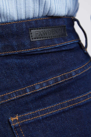 Close-up of the back pocket and waistband of a person wearing the Foxwood Sarah Wide Leg Jean in dark blue with orange stitching. A black leather patch above the pocket displays the brand name "FXWDENIM." The person is also wearing a light blue sweater.