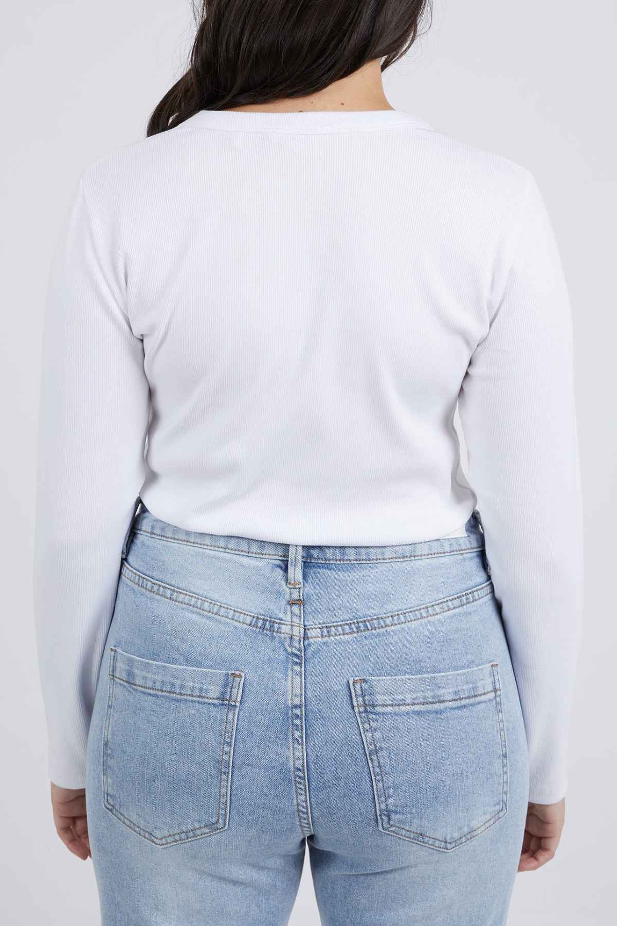 A person with long dark hair is shown from behind, wearing a white Foxwood Scoop Long Sleeve Rib and light blue denim jeans with visible back pockets. The background is plain white.