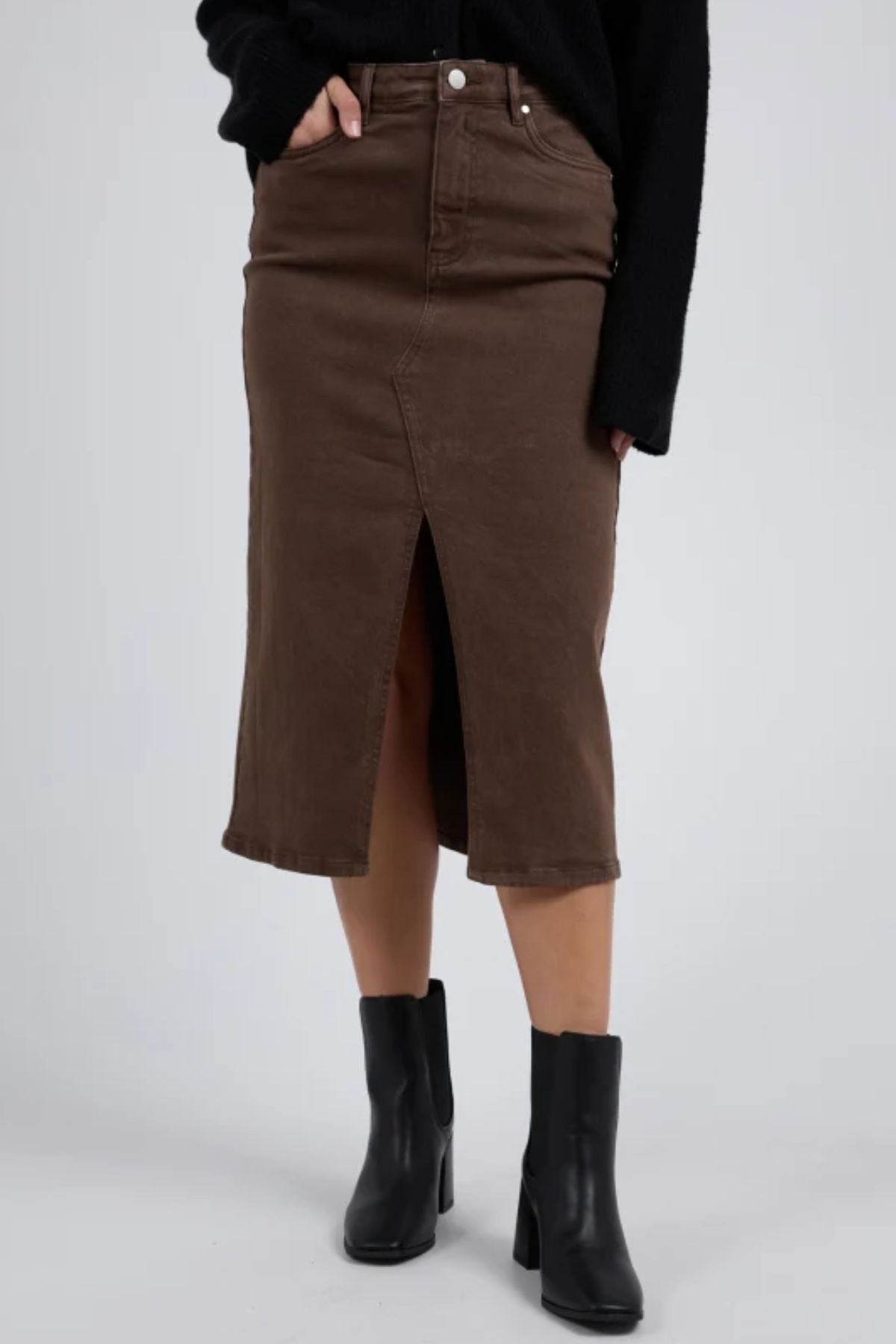 A person wearing the Foxwood Scout Midi Skirt in brown, paired with a black long-sleeve top and black heeled ankle boots, stands against a plain light grey background.