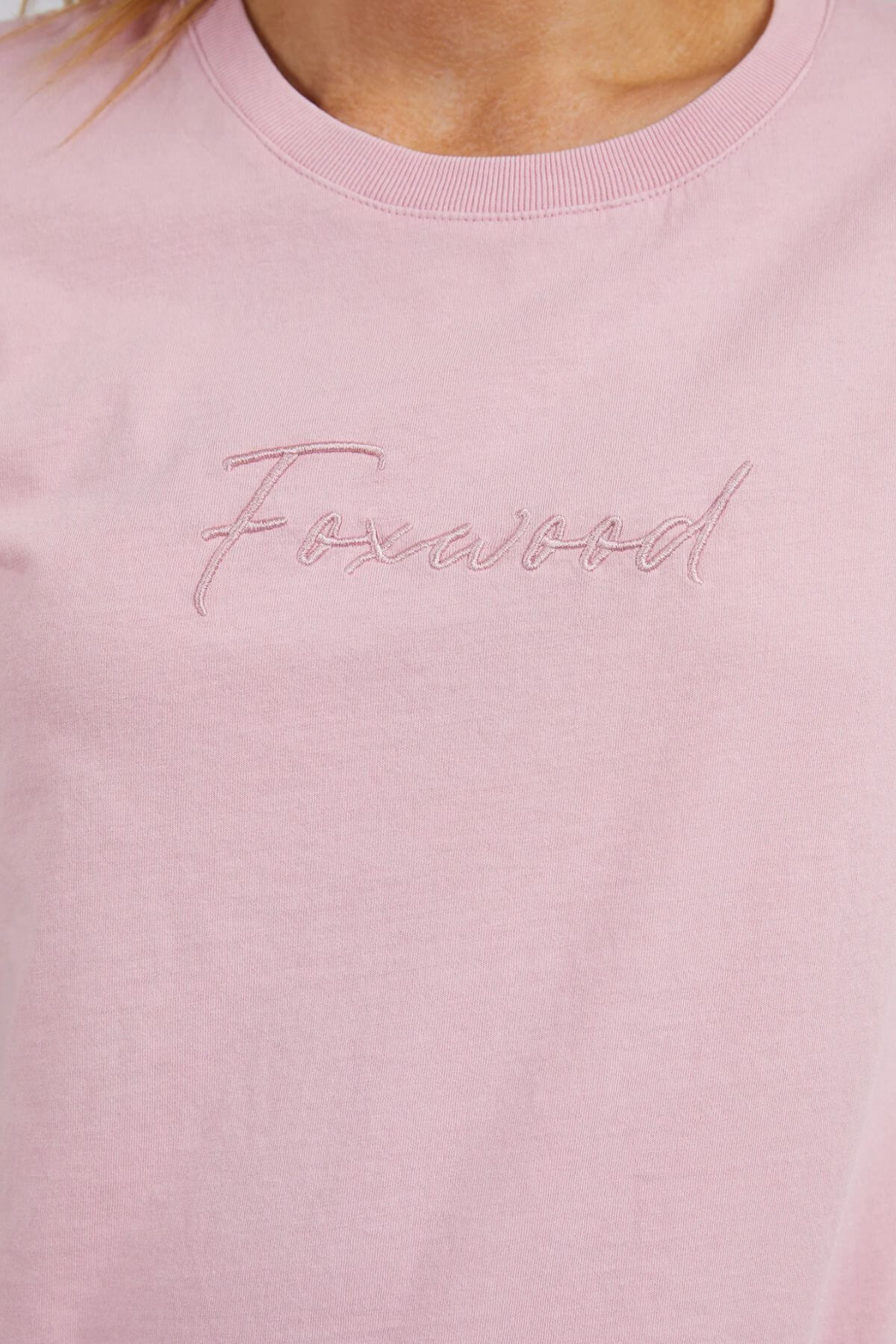 Close-up of the Foxwood Signature Tee, a light pink casual top featuring "Foxwood" embroidered in cursive on the chest. Crafted from 100% cotton for all-day comfort.