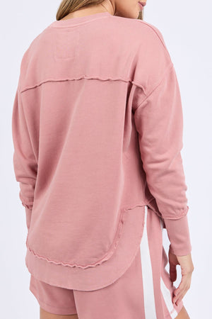 A person is shown from the back wearing the Foxwood Simplified Crew, a relaxed fit 100% cotton sweater in dusty pink with visible seams, paired with matching pink shorts with a white stripe, set against a plain background.