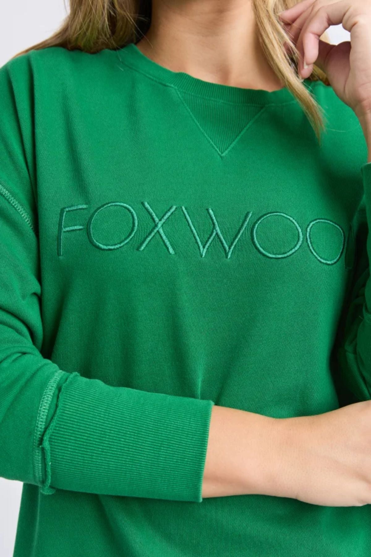 A person wears a relaxed fit, bright green Foxwood Simplified Crew, featuring "FOXWOOD" embroidered on the chest. Only their lower face, neck, and upper body are shown.
