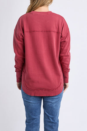 A woman with long, light brown hair is seen from the back wearing a Foxwood Simplified Crew sweatshirt with blue jeans, standing against a plain light background.