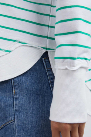 Close-up of a person wearing blue denim jeans and the Foxwood Simplified Stripe Crew, a relaxed fit 100% cotton sweater with green horizontal stripes and ribbed cuffs, slightly overlapping the jeans at the hip.