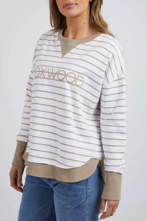 A person is wearing the Foxwood Simplified Stripe Crew in white and tan, showcasing "FOXWOOD" on the front. This relaxed-fit, 100% cotton sweatshirt with tan cuffs and collar is paired with blue jeans against a plain white background.