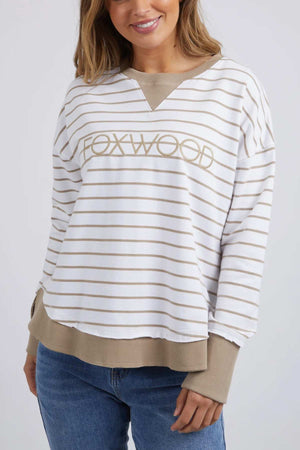 The woman sports the Foxwood Simplified Stripe Crew sweatshirt, featuring a relaxed fit in white and tan stripes and crafted from 100% cotton with "FOXWOOD" on the front. She pairs it effortlessly with blue jeans for a stylishly casual look.