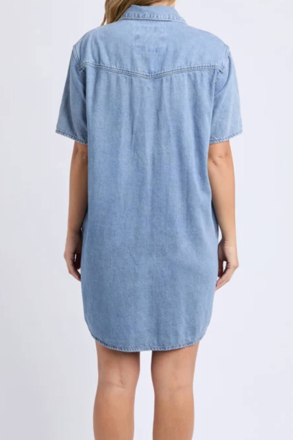 A person is shown from the back wearing the Foxwood Sorcha Denim Dress, a short-sleeved, light blue denim shirt dress with an above-the-knee length. The background is plain white.